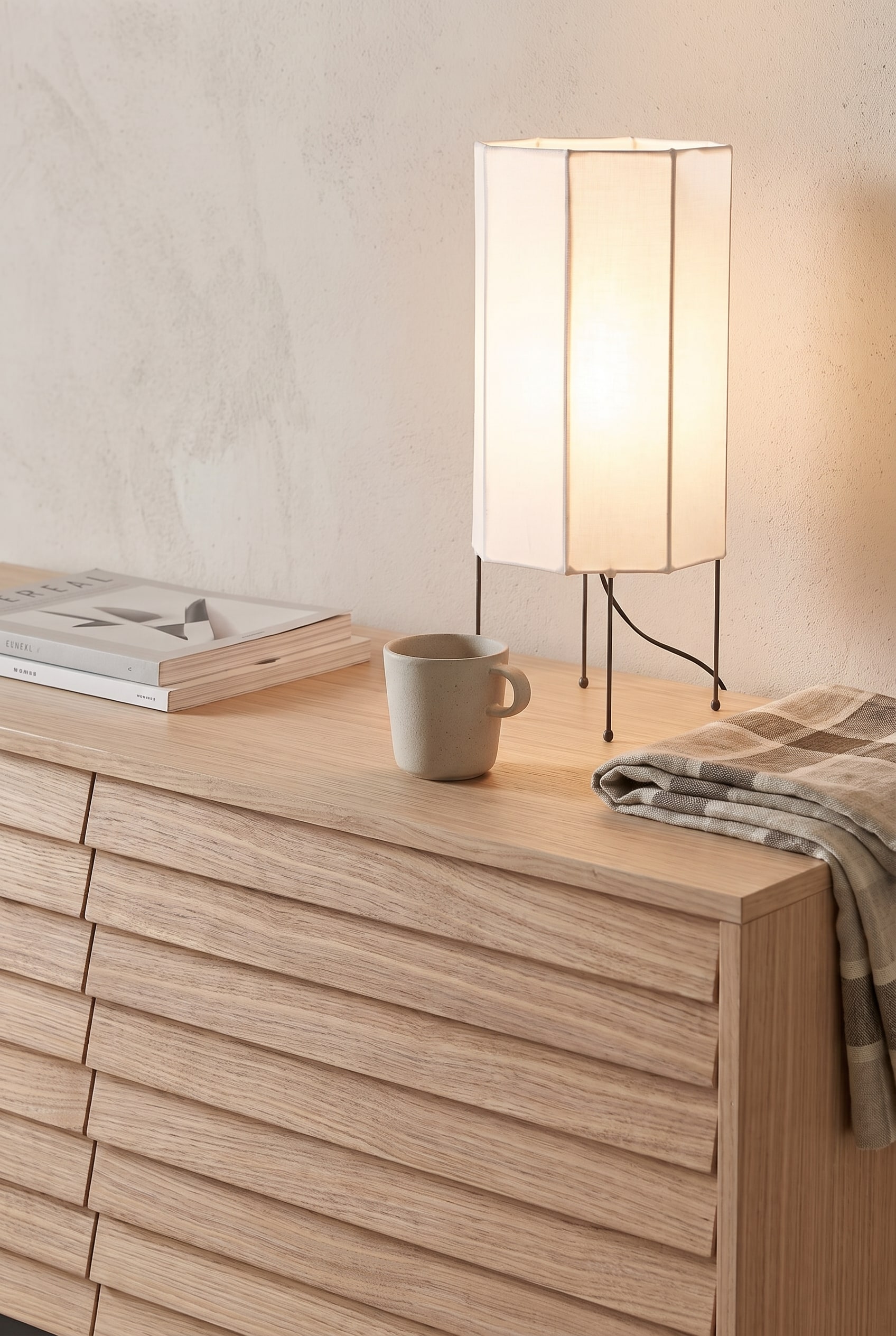 Gros plan d'un sideboard clair en bois de fr&ecirc;ne avec une structure &agrave; lamelles verticales, d&eacute;cor&eacute; d'une d&eacute;licate lampe en papier et d'un vase en verre.