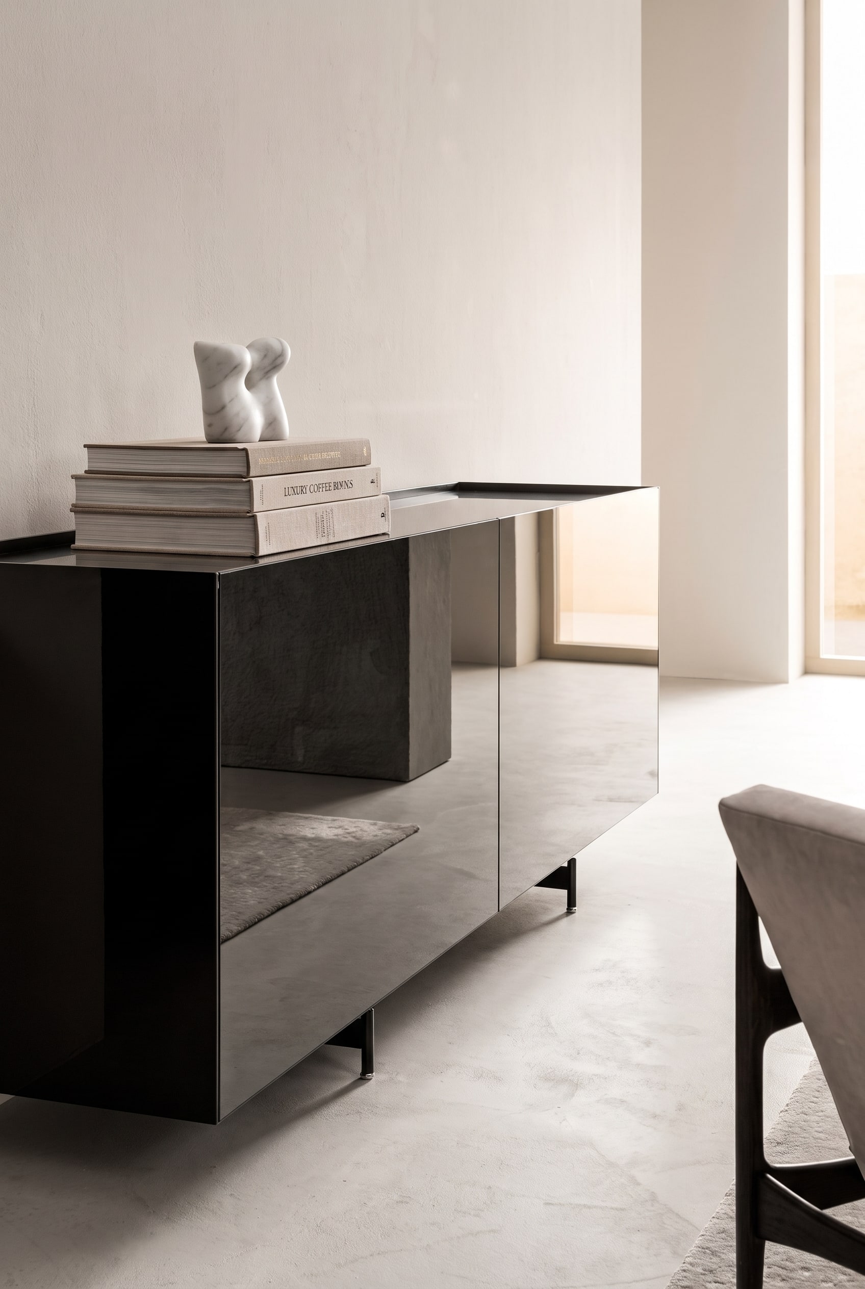 Sideboard avec fa&ccedil;ades miroir, surmont&eacute; d'une pile ordonn&eacute;e de trois grands livres d'art, couronn&eacute;e d'une petite sculpture en marbre blanc
