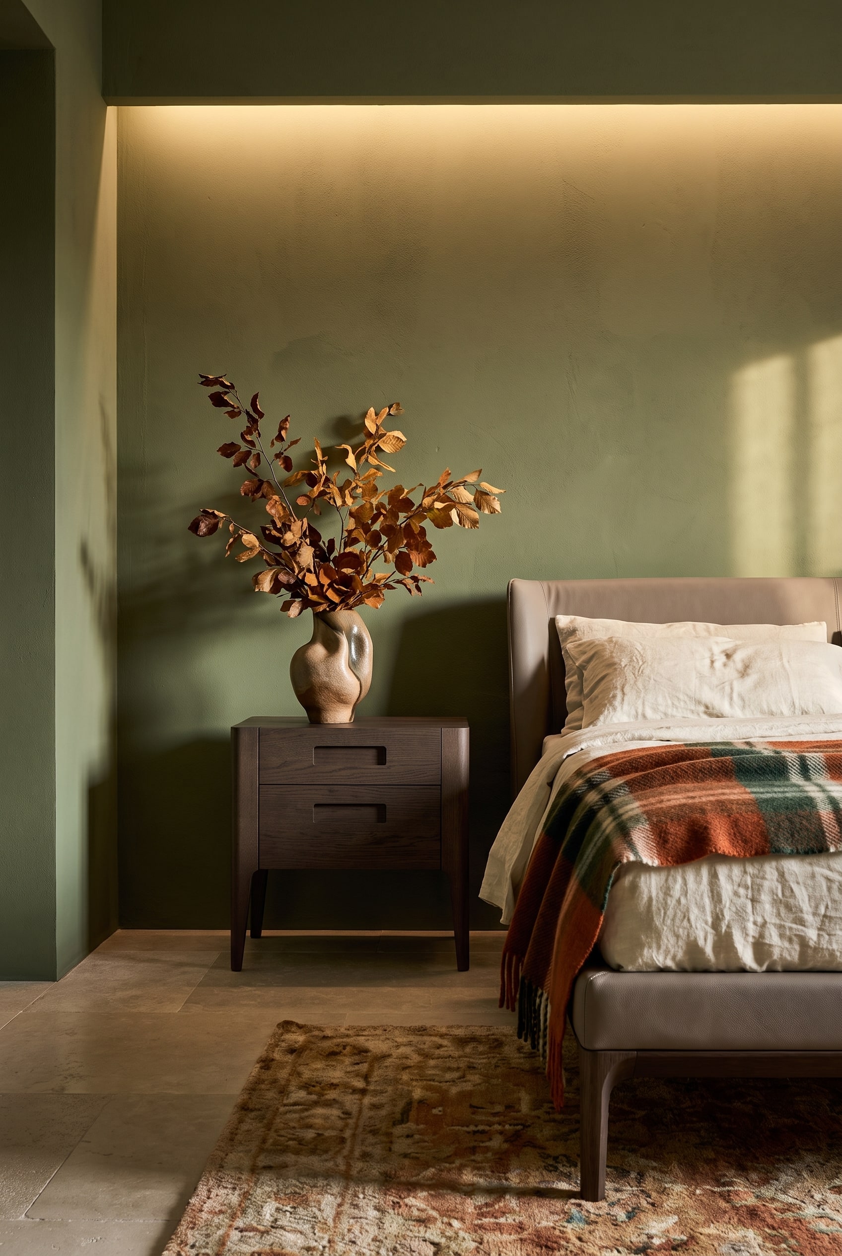 Ein dunkler Nussbaum-Nachttisch mit zwei Schubladen steht stilvoll vor einer matt-olivgr&uuml;nen Wand in einem eleganten Herbst-Schlafzimmer.