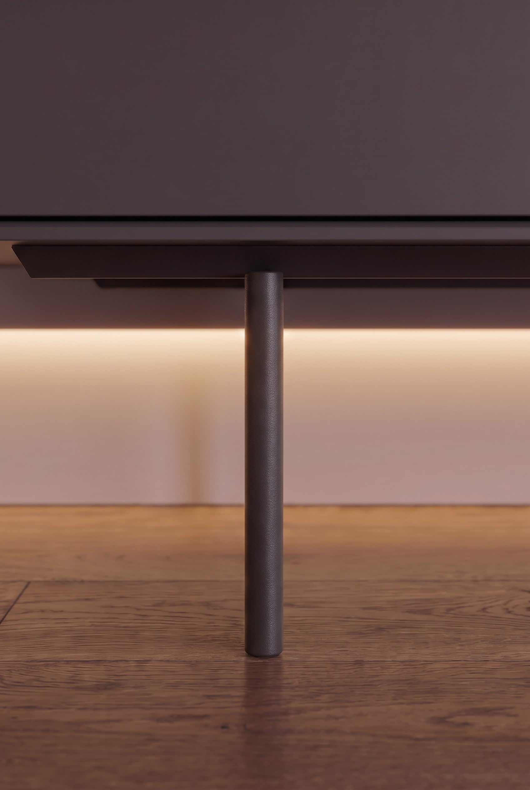 Gros plan d'un pied m&eacute;tallique cylindrique &eacute;troit d'un buffet avec &eacute;clairage indirect sous le meuble sur parquet en bois.