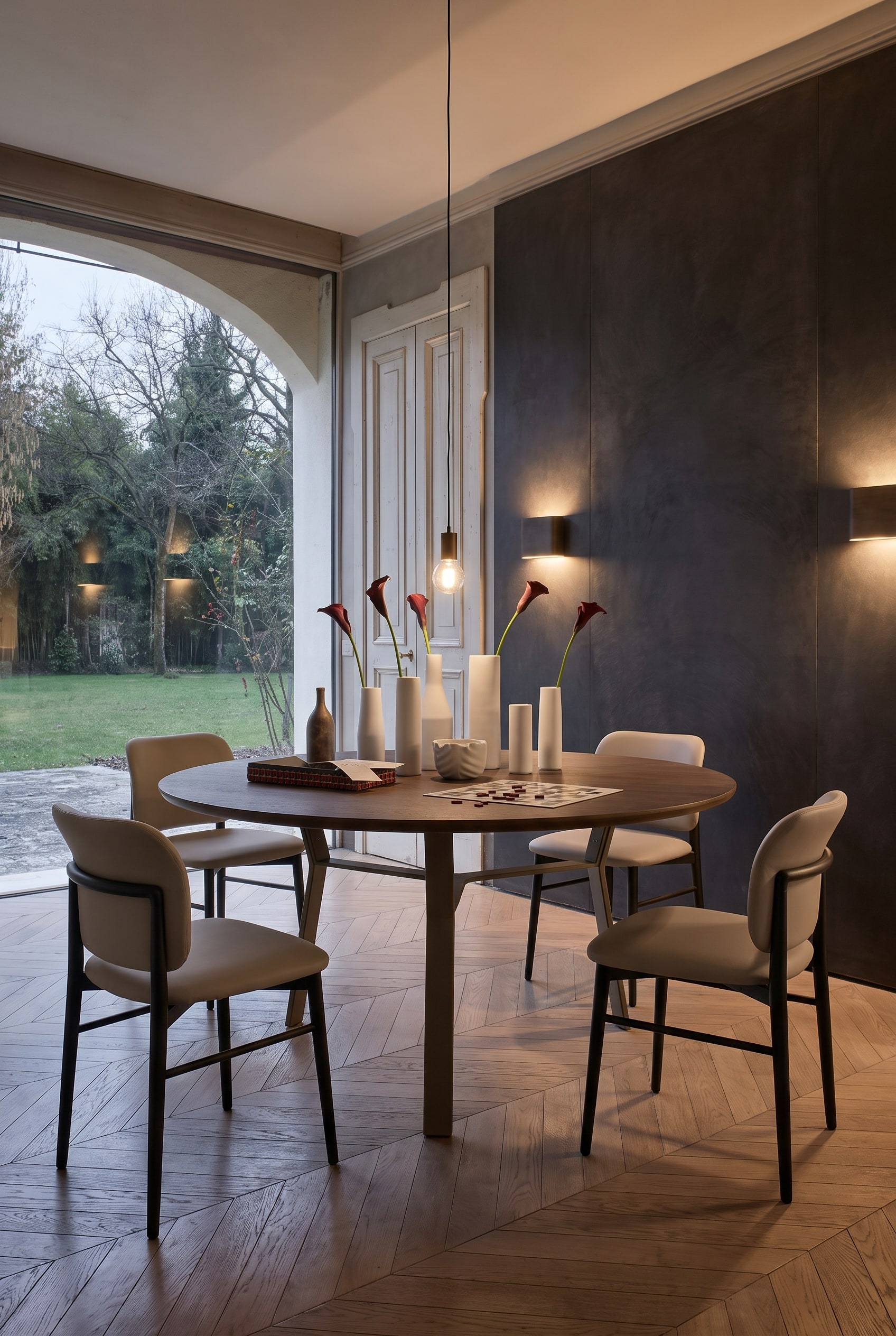 Élégante salle à manger avec mur sombre, longue table à manger avec piètement métallique et élégantes chaises en cuir couleur taupe