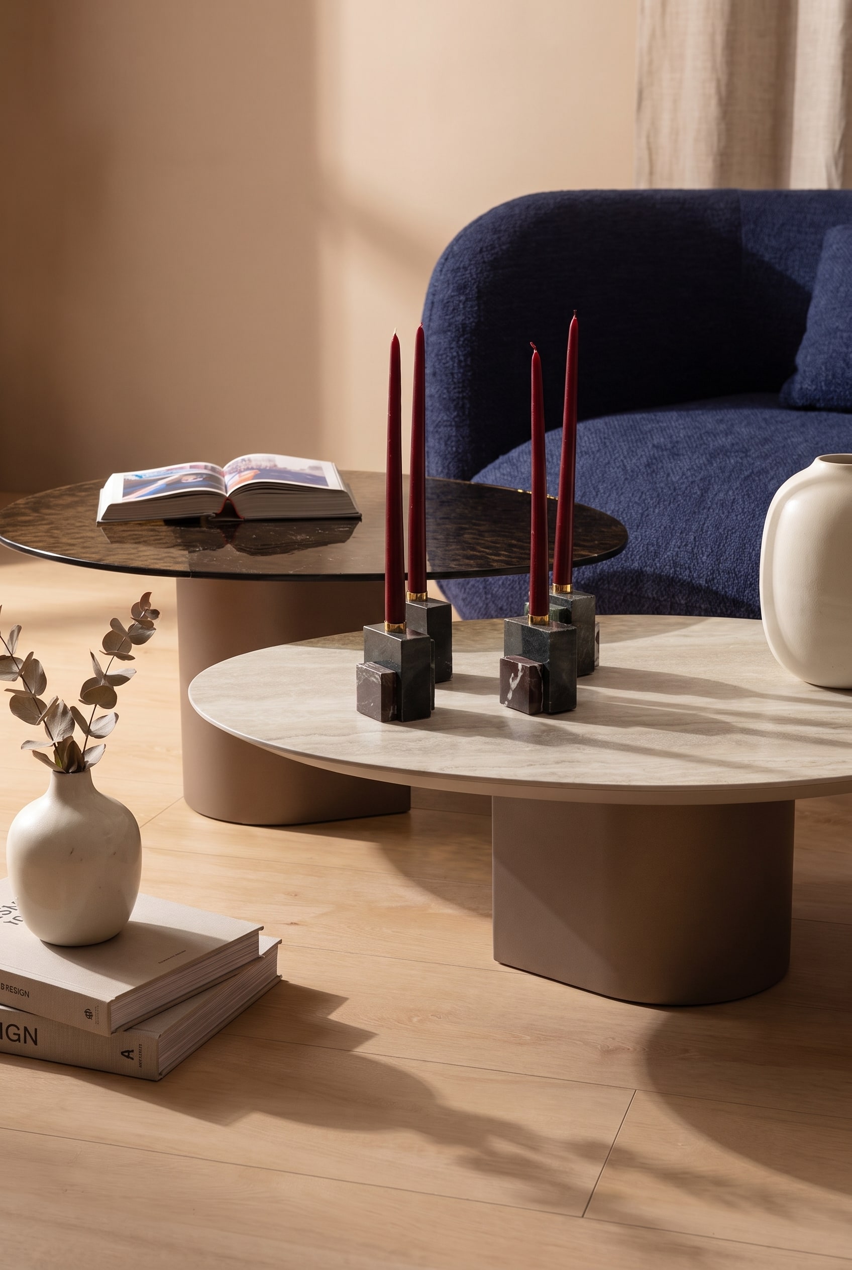 Gros plan d'une table basse ronde en bois clair avec d&eacute;coration en c&eacute;ramique devant un canap&eacute; en tissu bleu fonc&eacute;