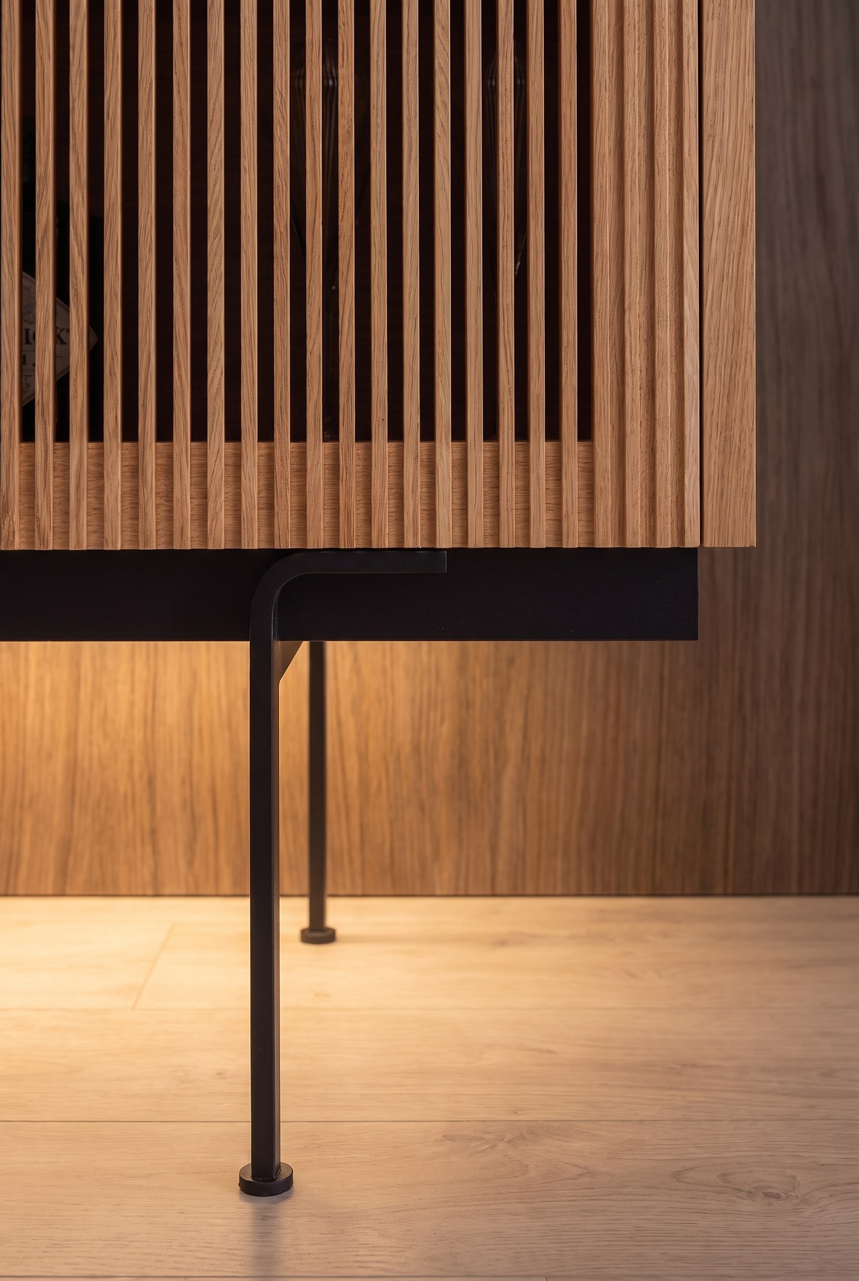 Detailaufnahme des schwarzen Metallbeins eines Highboards mit warmer indirekter Fußbodenbeleuchtung.