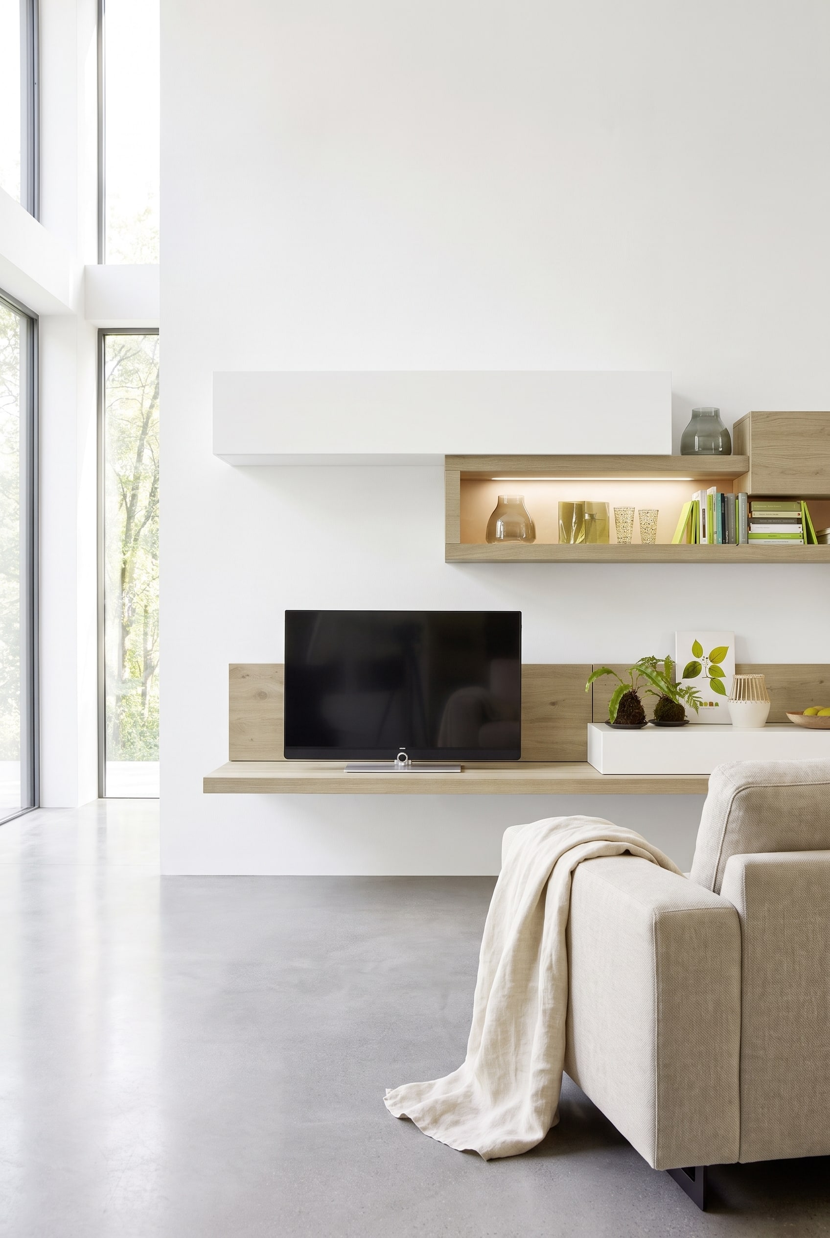 Meuble TV bas moderne en bois aspect ch&ecirc;ne sauvage devant un mur en b&eacute;ton froid, combin&eacute; avec un plaid en lin textur&eacute;.