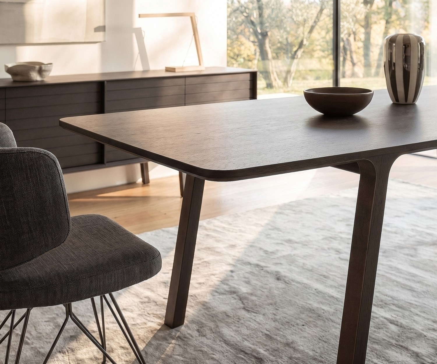 Table de salle à manger mobius 001 par al2 en eucalyptus foncé dans un séjour moderne avec chaise design et tapis clair.