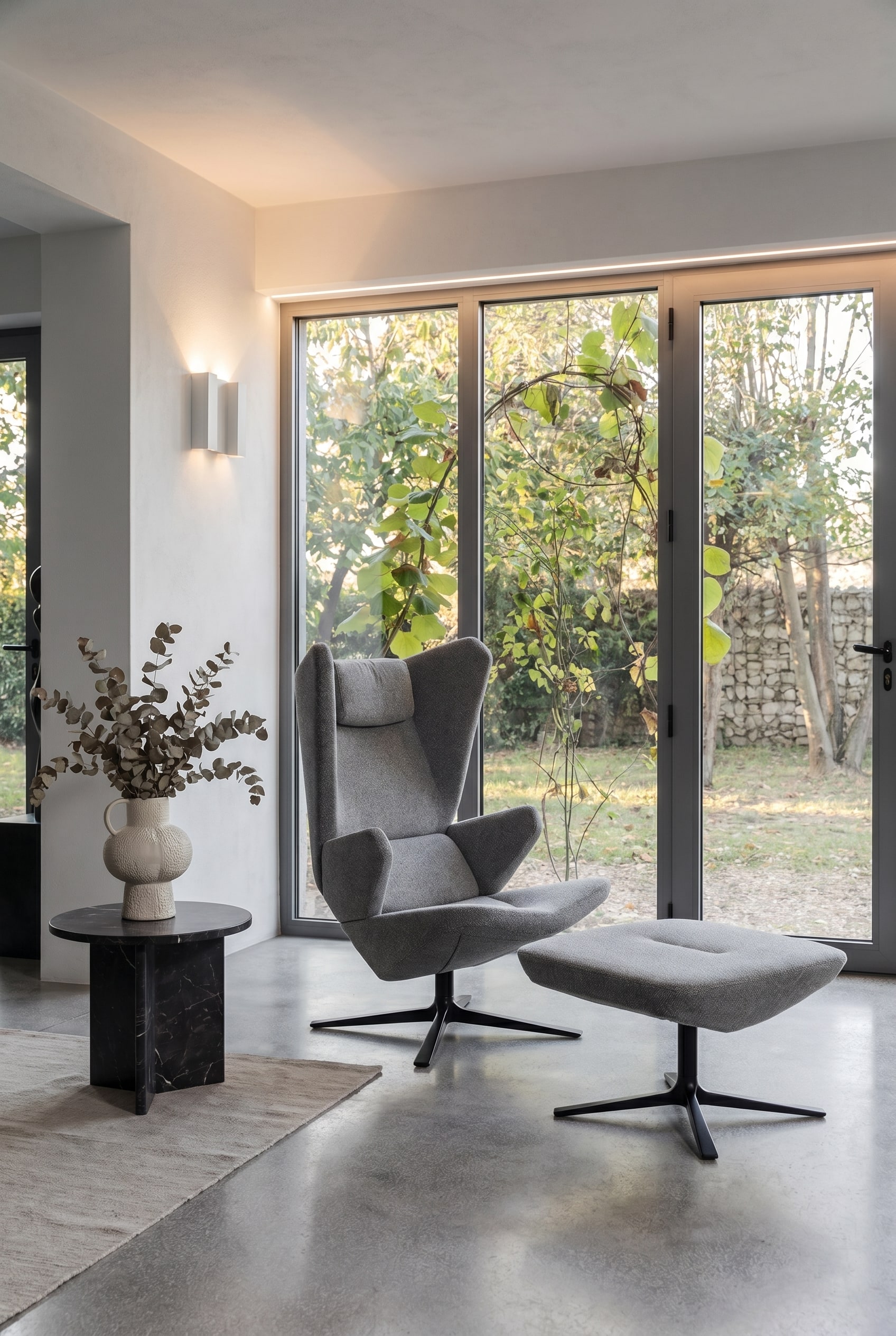 Modernes Wohnzimmer mit Sessel Trifidae in grauem Strukturstoff, Beistelltisch mit Keramikvase und gro&szlig;fl&auml;chigen Fenstern