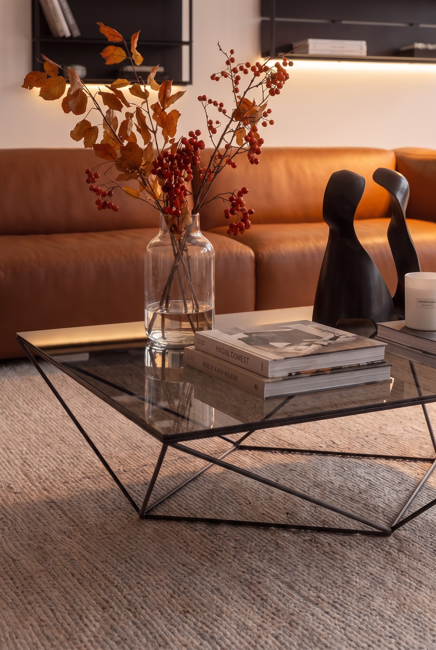 Gros plan d'une table basse filigrane avec pi&egrave;tement en m&eacute;tal mat et plateau en verre fum&eacute; teint&eacute; devant des meubles rembourr&eacute;s doux.