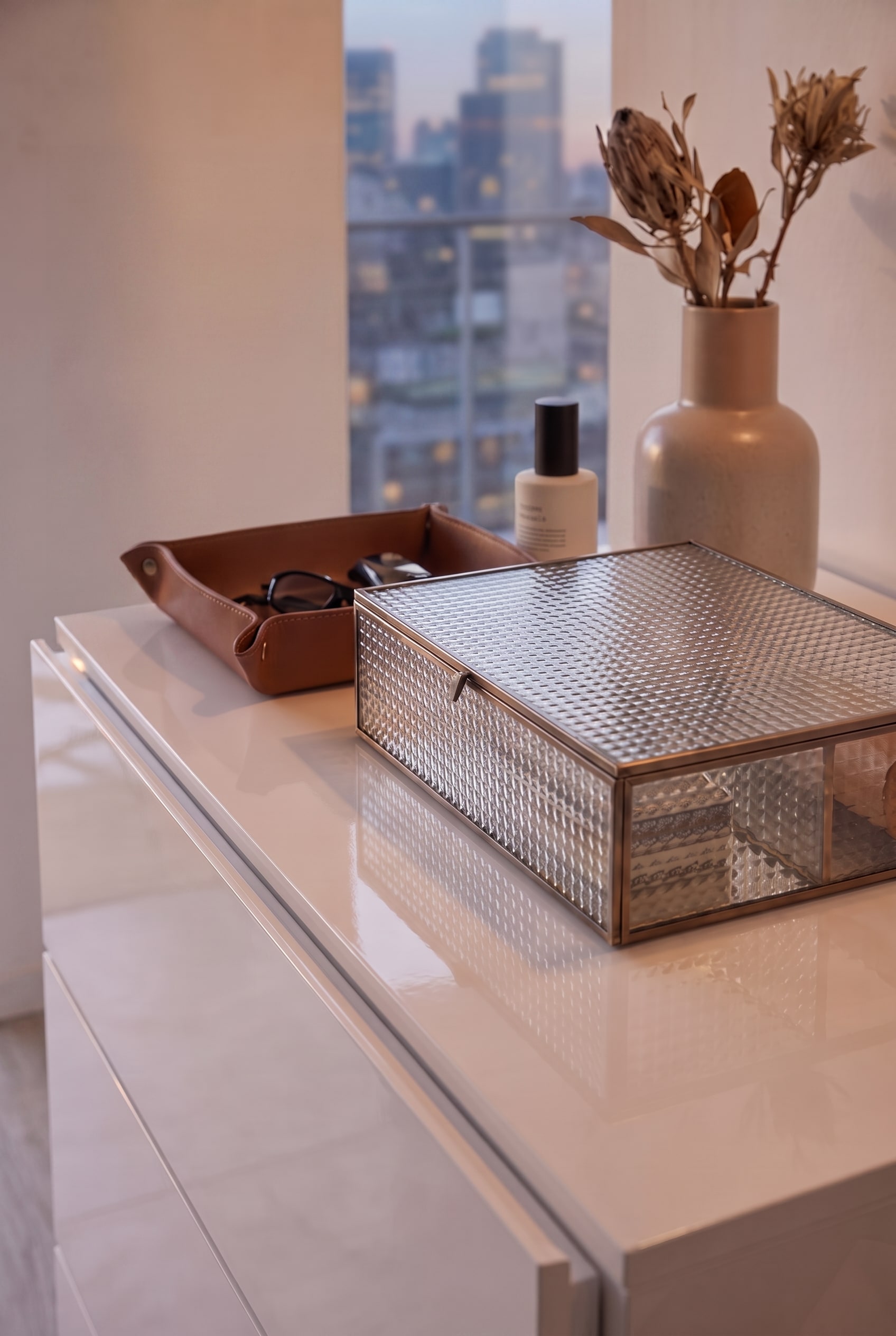 Vue de dessus d'une commode blanche brillante avec boîte en verre et plateau en cuir, mise en scène de manière puriste sans tringle à vêtements.