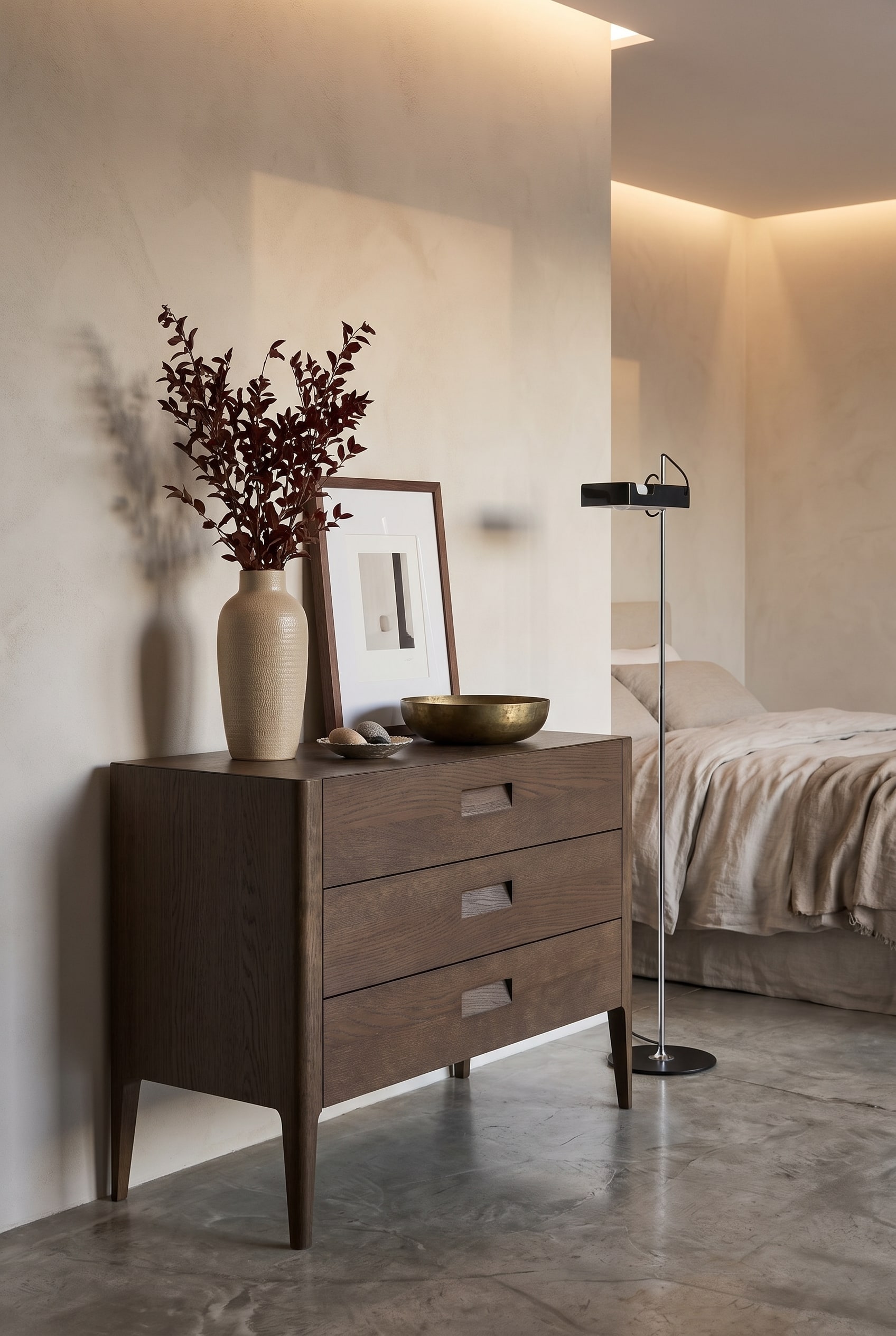 Chambre moderne avec commode en ch&ecirc;ne fonc&eacute;, grand vase en c&eacute;ramique, cadre photo de taille moyenne et coupelle en laiton plate dans une lumi&egrave;re chaude