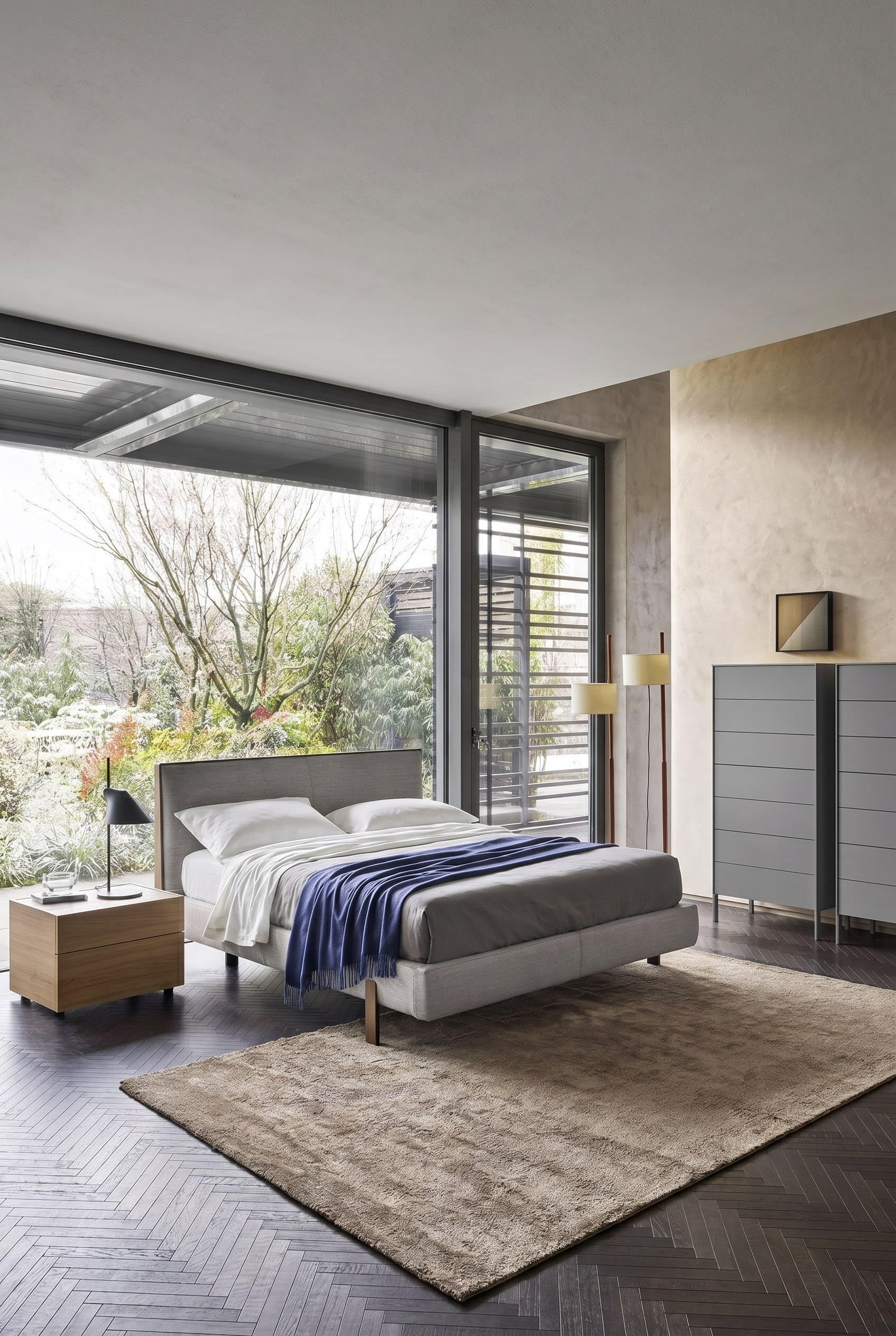 Elegantes Schlafzimmer mit bodentiefen Fenstern und einer modernen grauen Hochkommode auf schlanken Metallf&uuml;&szlig;en