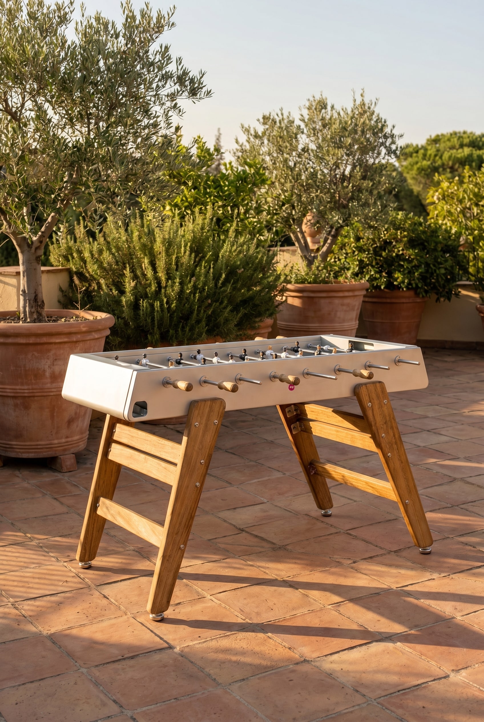 Mediterrane Terrasse mit Iroko-Holz Tischkicker und gro&szlig;en Pflanzk&uuml;beln im warmen Abendlicht