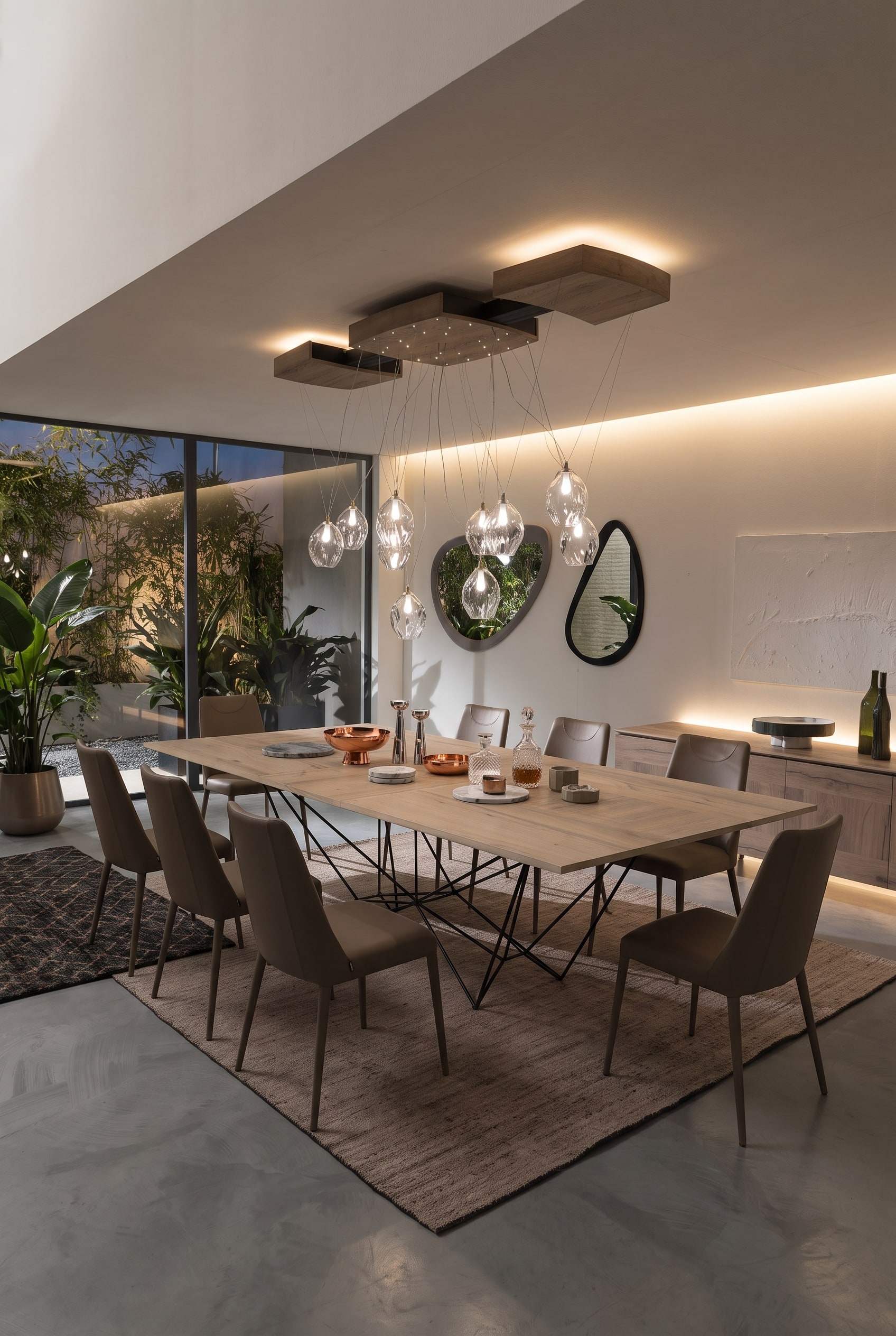 Salle &agrave; manger ouverte moderne avec une grande table &agrave; manger sur un pi&egrave;tement m&eacute;tallique g&eacute;om&eacute;trique, quatre chaises taupe et un buffet en bois