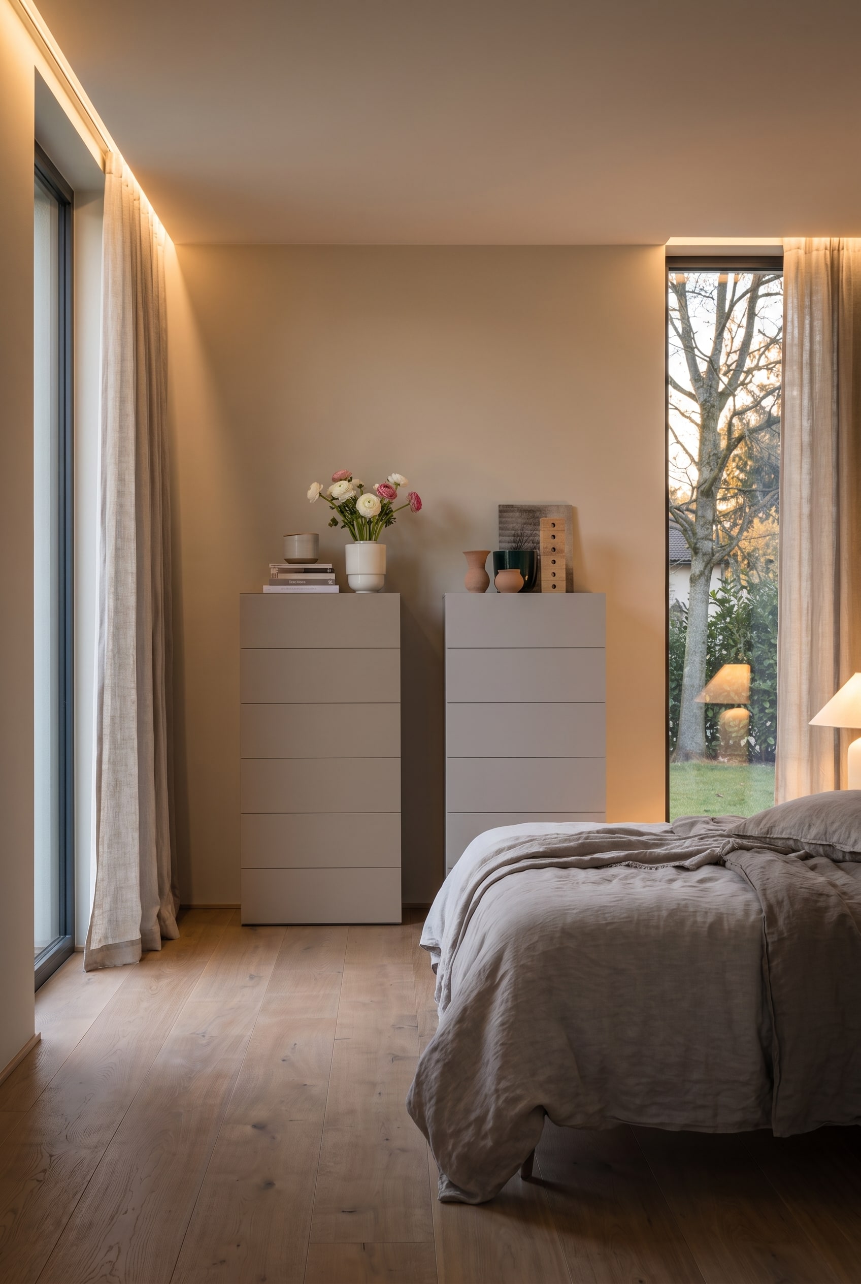 Deux commodes hautes greige dans une chambre moderne avec linge de lit en lin et fen&ecirc;tres pleine hauteur.