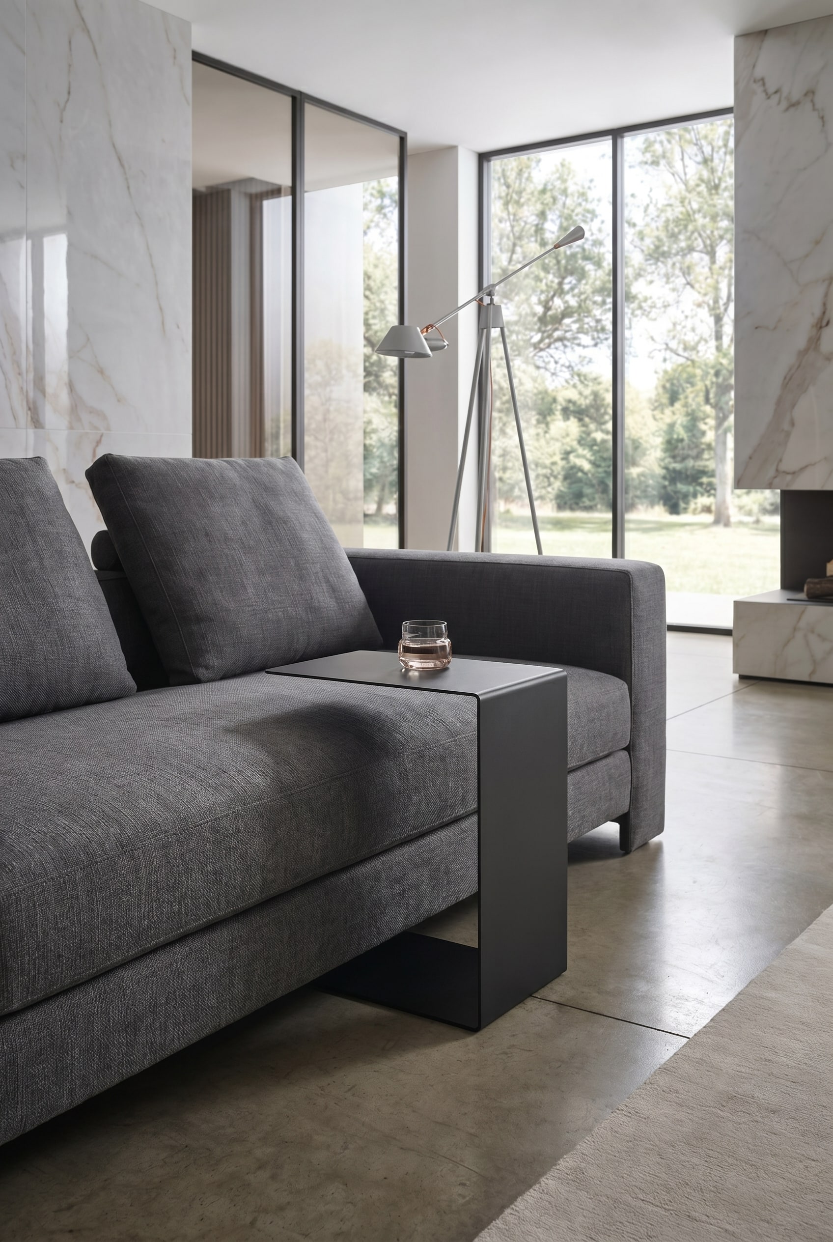 Detailaufnahme eines grauen Stoffsofas mit einem schwarzen, minimalistischen C-f&ouml;rmigen Beistelltisch aus Metall
