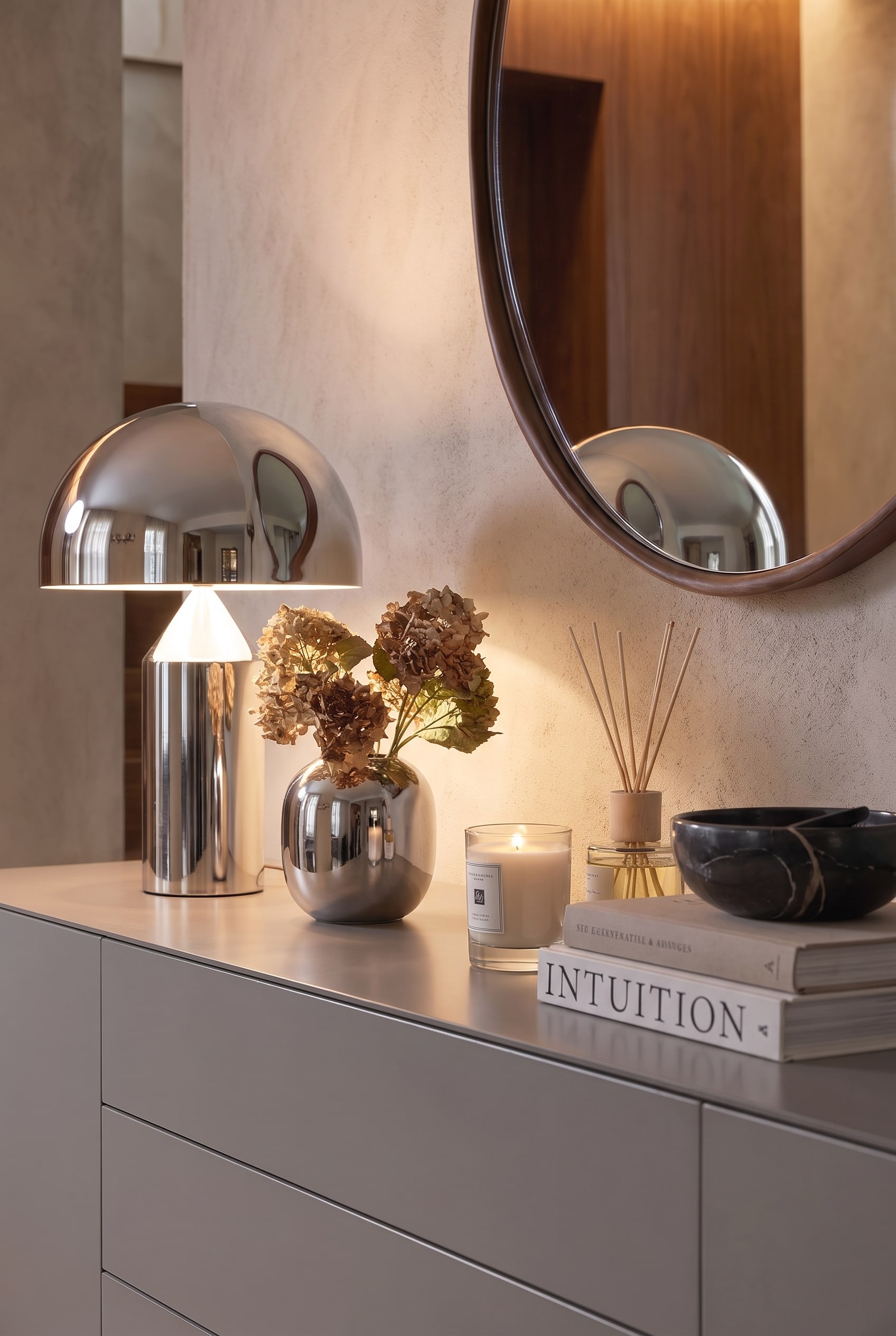Gros plan sur la d&eacute;coration : Une lampe chrom&eacute;e brillante, un vase en argent avec des hortensias s&eacute;ch&eacute;s et une bougie allum&eacute;e sur une laque grise.