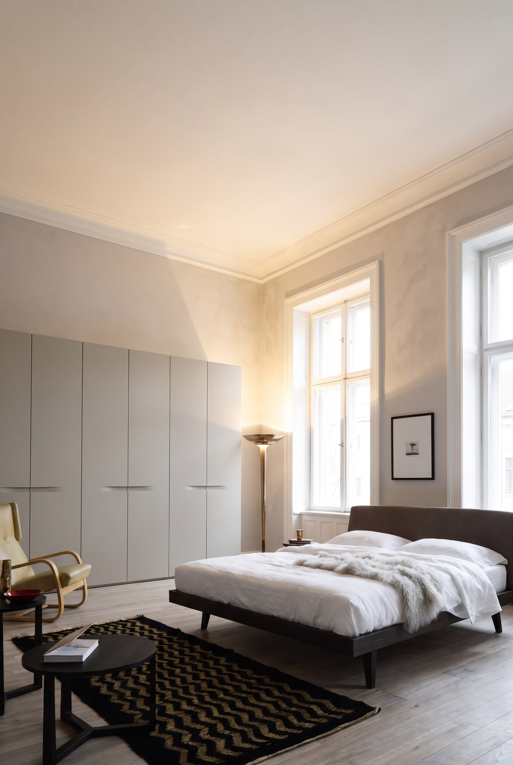 Elegantes Altbau-Schlafzimmer mit einem deckenhohen, matten Kleiderschrank, Holzbett und warmen Textilien