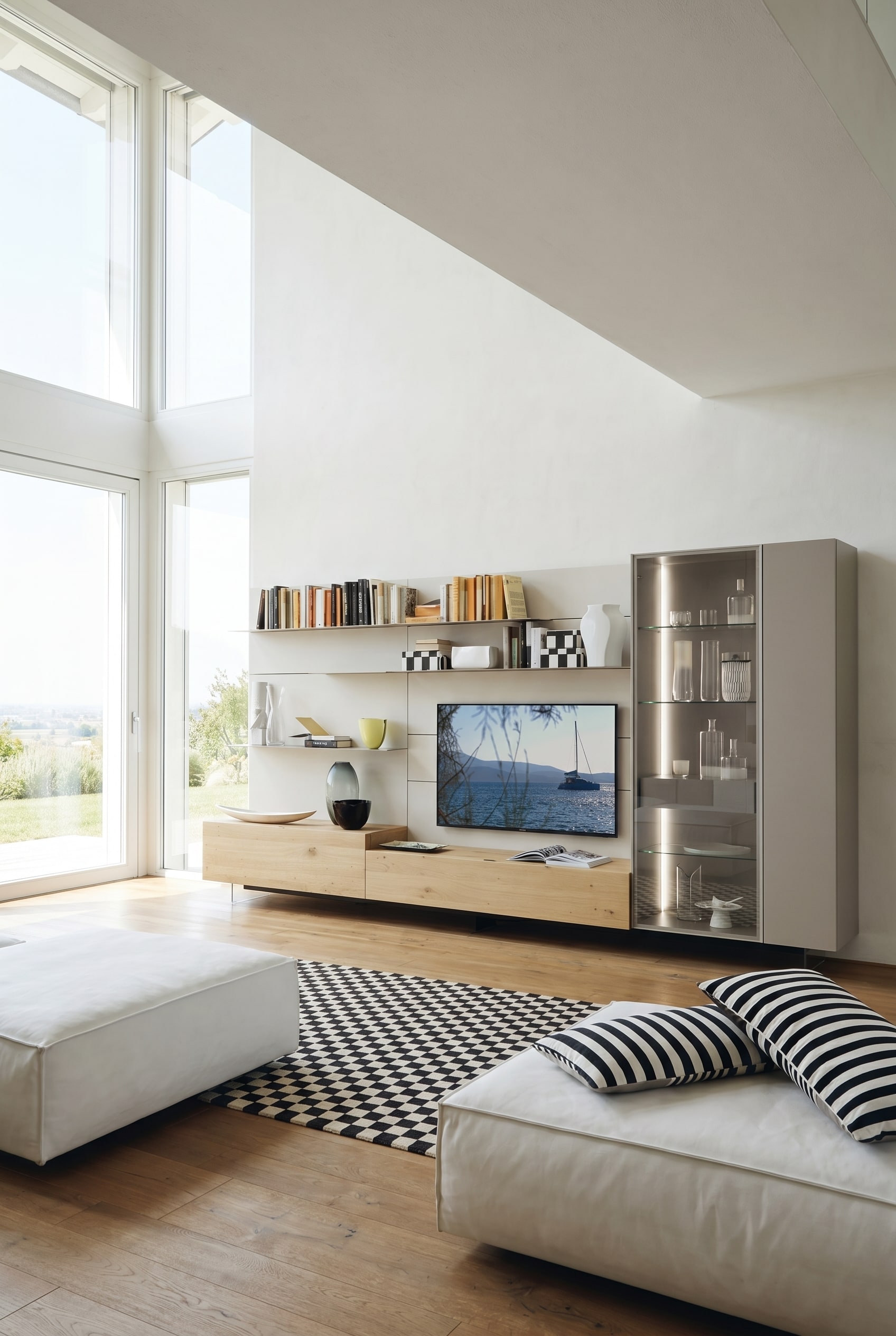 Salon lumineux avec modules de base flottants en ch&ecirc;ne clair, &eacute;tag&egrave;res blanches et une haute vitrine en verre &eacute;clair&eacute;e chaleureusement