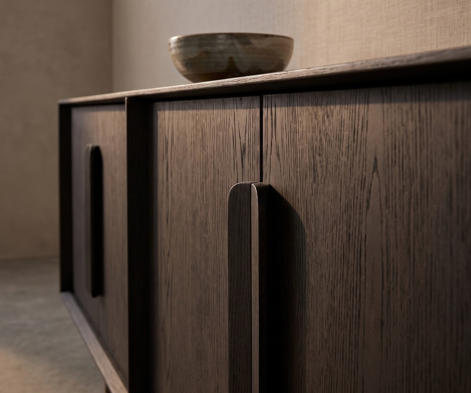 al2 Mobius 003 Sideboard aus dunkler Eiche al2 Mobius 003 Sideboard aus dunkler Carbone Eiche im Wohnzimmer mit edlen Holzgriffen und dekorativer Schale im Detail.
