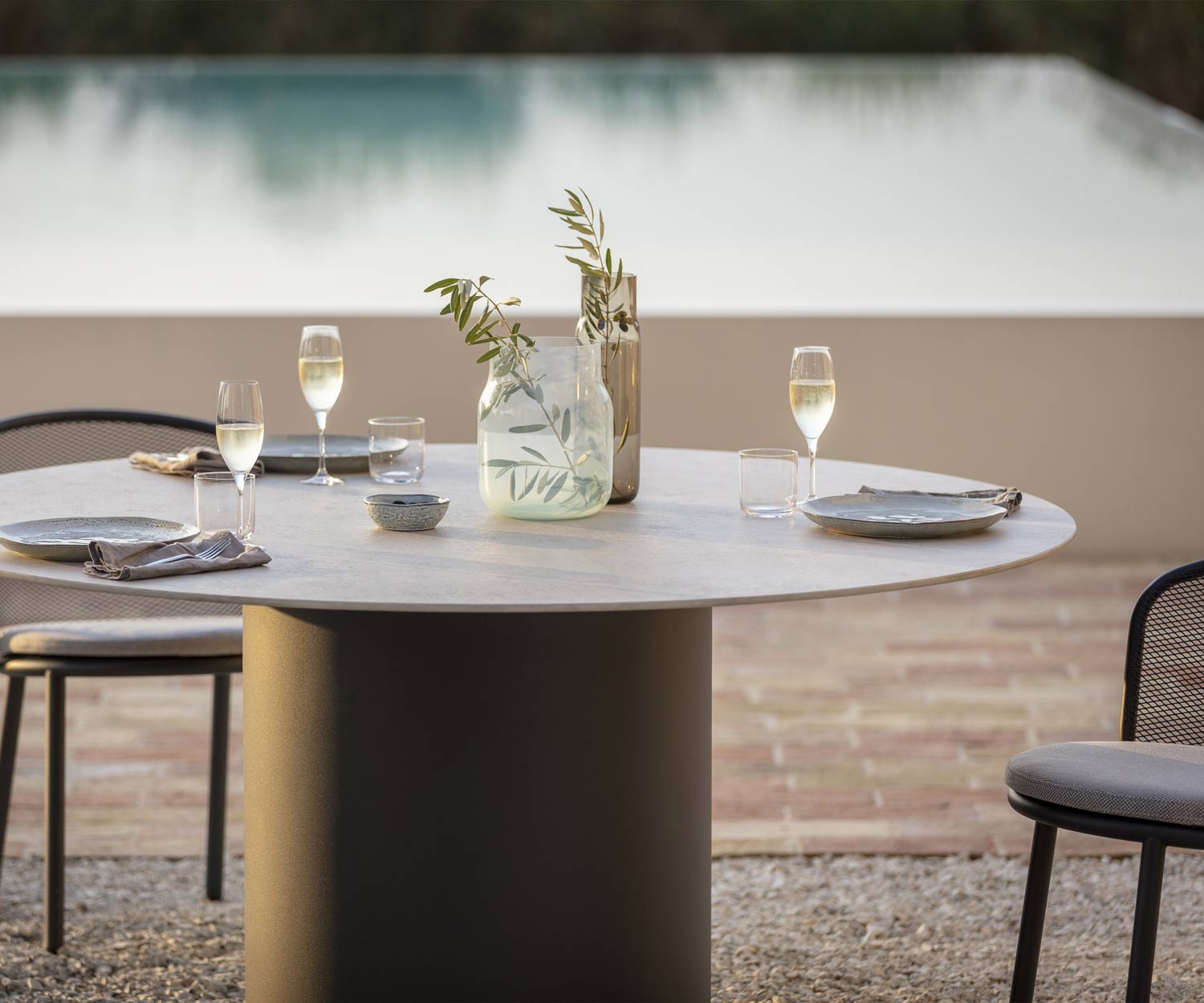 Table de salle à manger couverte de Todus avec plateau de table en céramique grise au bord de la piscine sur une terrasse de gravier