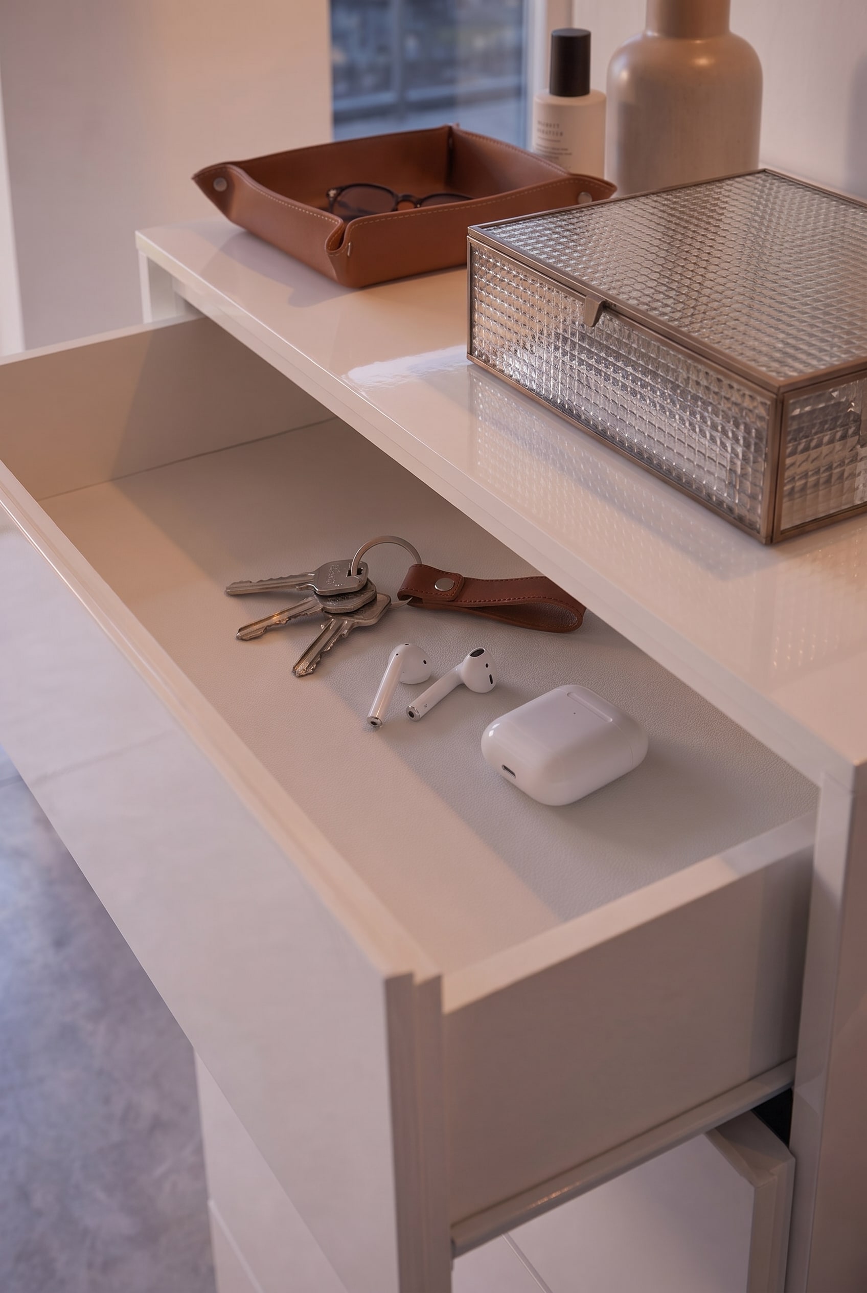 Tiroir plat ouvert d'une commode blanche, contenant des cl&eacute;s, des AirPods et un porte-cl&eacute;s en cuir rang&eacute;s.