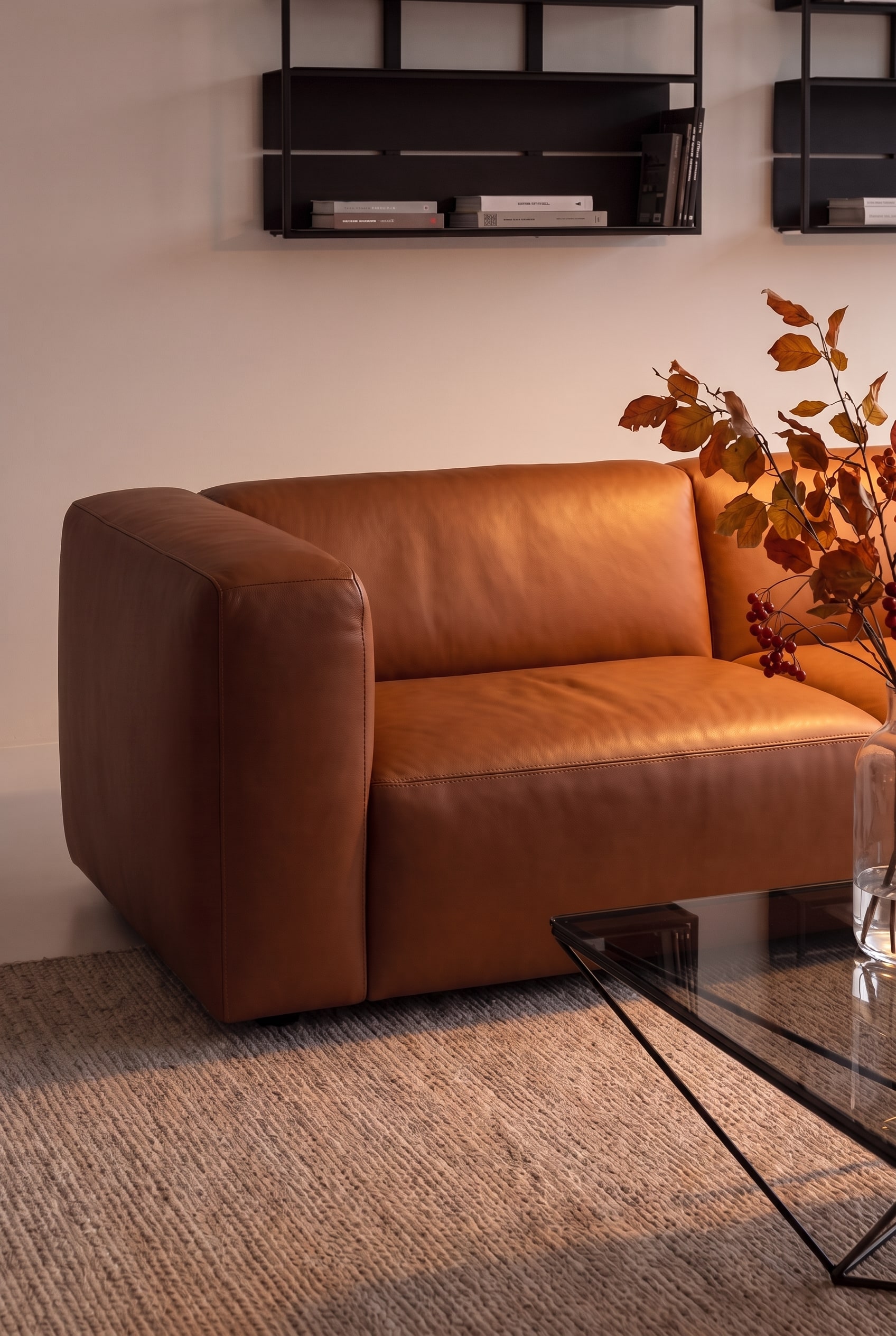 Gros plan de l'accoudoir lisse et sans couture d'un canapé en cuir couleur cognac, éclairé par une lumière chaude.