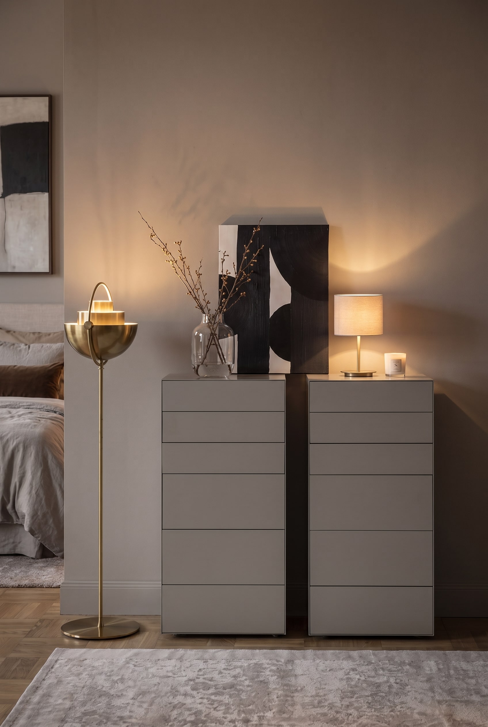 Frontale Ansicht zweier grauer Hochkommoden mit asymmetrischer Dekoration und einer goldenen Stehlampe links.