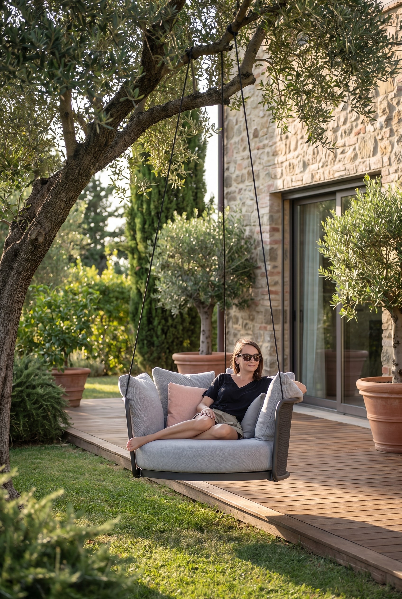 Bord de terrasse vert avec un fauteuil suspendu gris flottant, fixé à une structure moderne à l'ombre fraîche d'un arbre