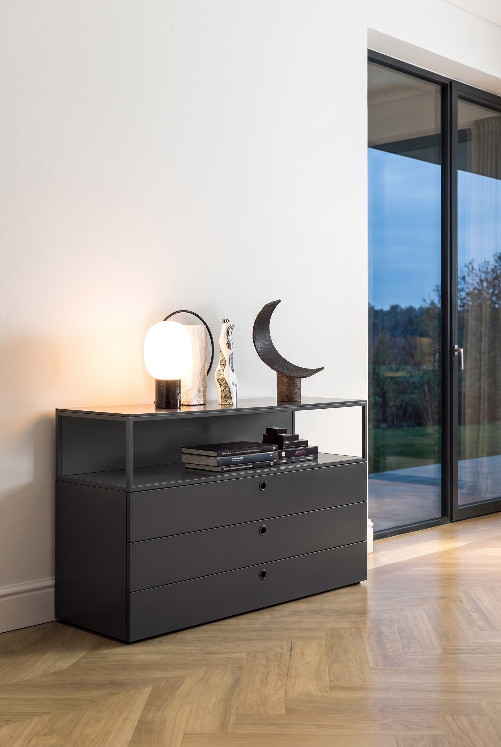 Modernes Wohnzimmer mit tiefschwarzer matter Kommode vor wei&szlig;er Wand auf hellem Holzboden