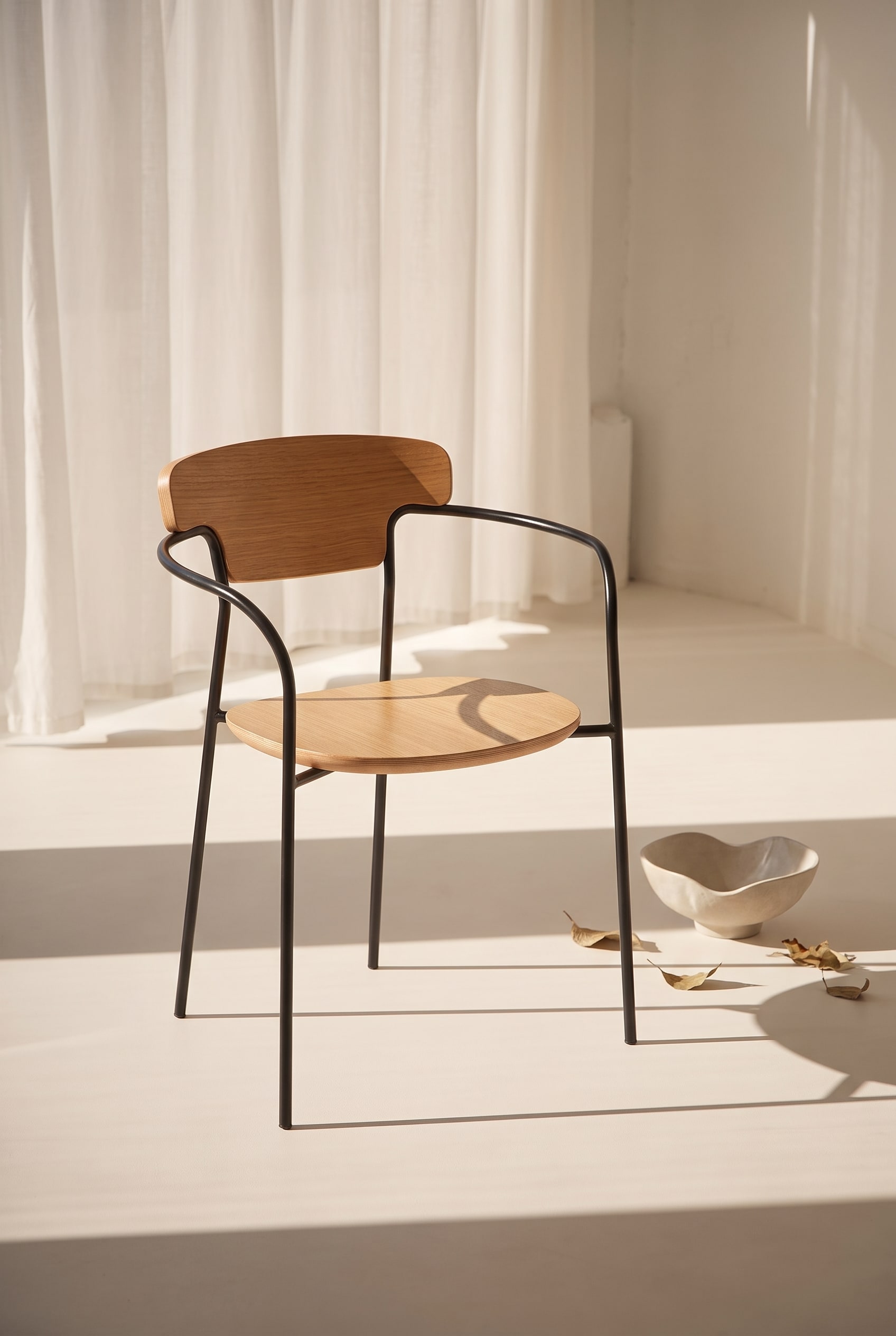 Pi&egrave;ce lumineuse avec une chaise de salle &agrave; manger en bois de ch&ecirc;ne avec un dossier incurv&eacute; et une structure en m&eacute;tal noir